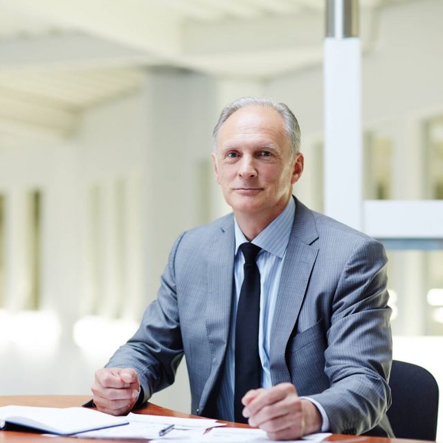 Director of company Mature boss in formalwear sitting by his workplace in office and planning work