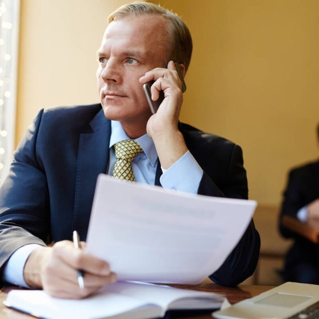 Business leader with document consulting client by cellphone